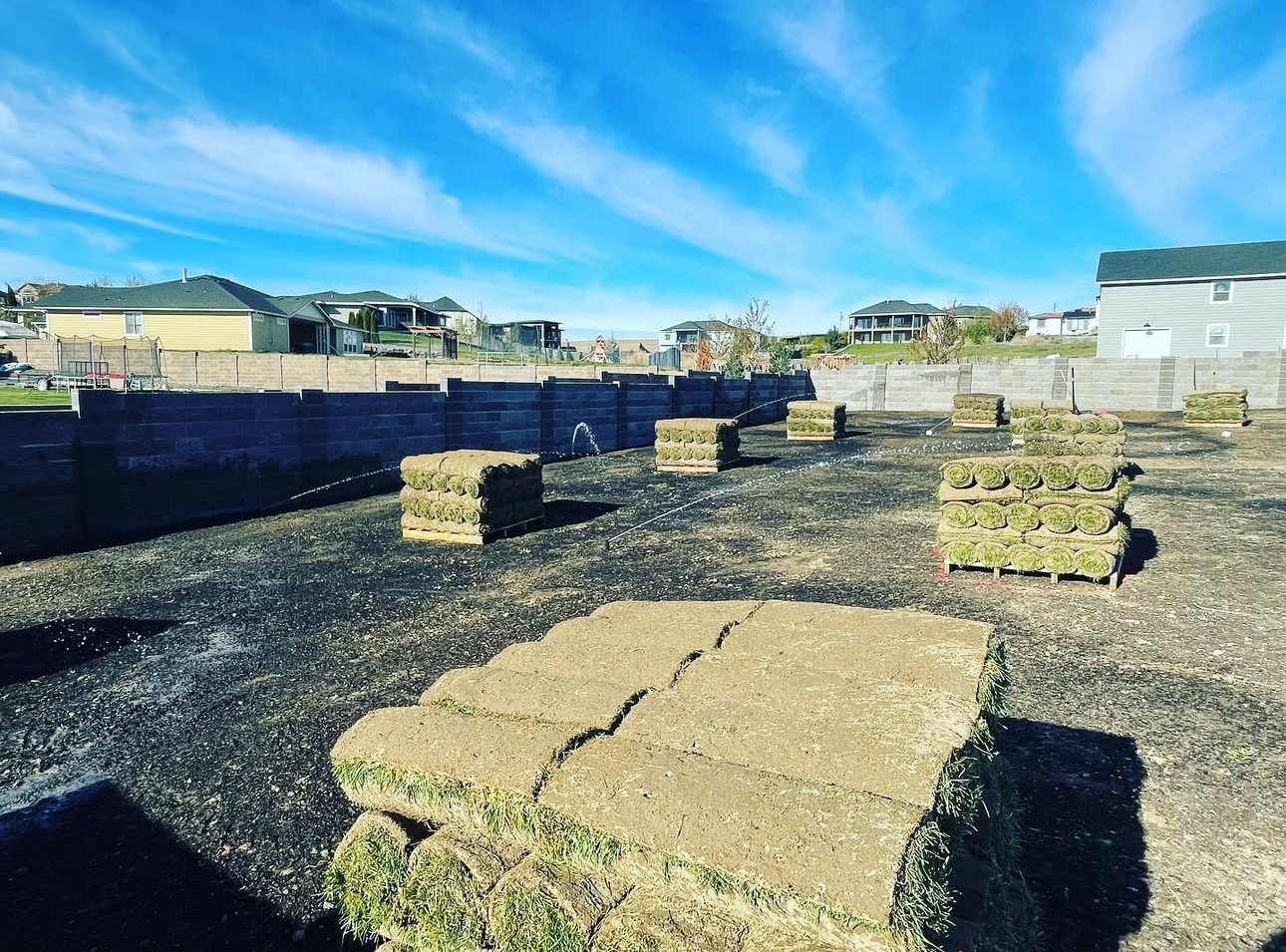 Freshly graded backyard with pallets of sod staged and irrigation running in Pasco