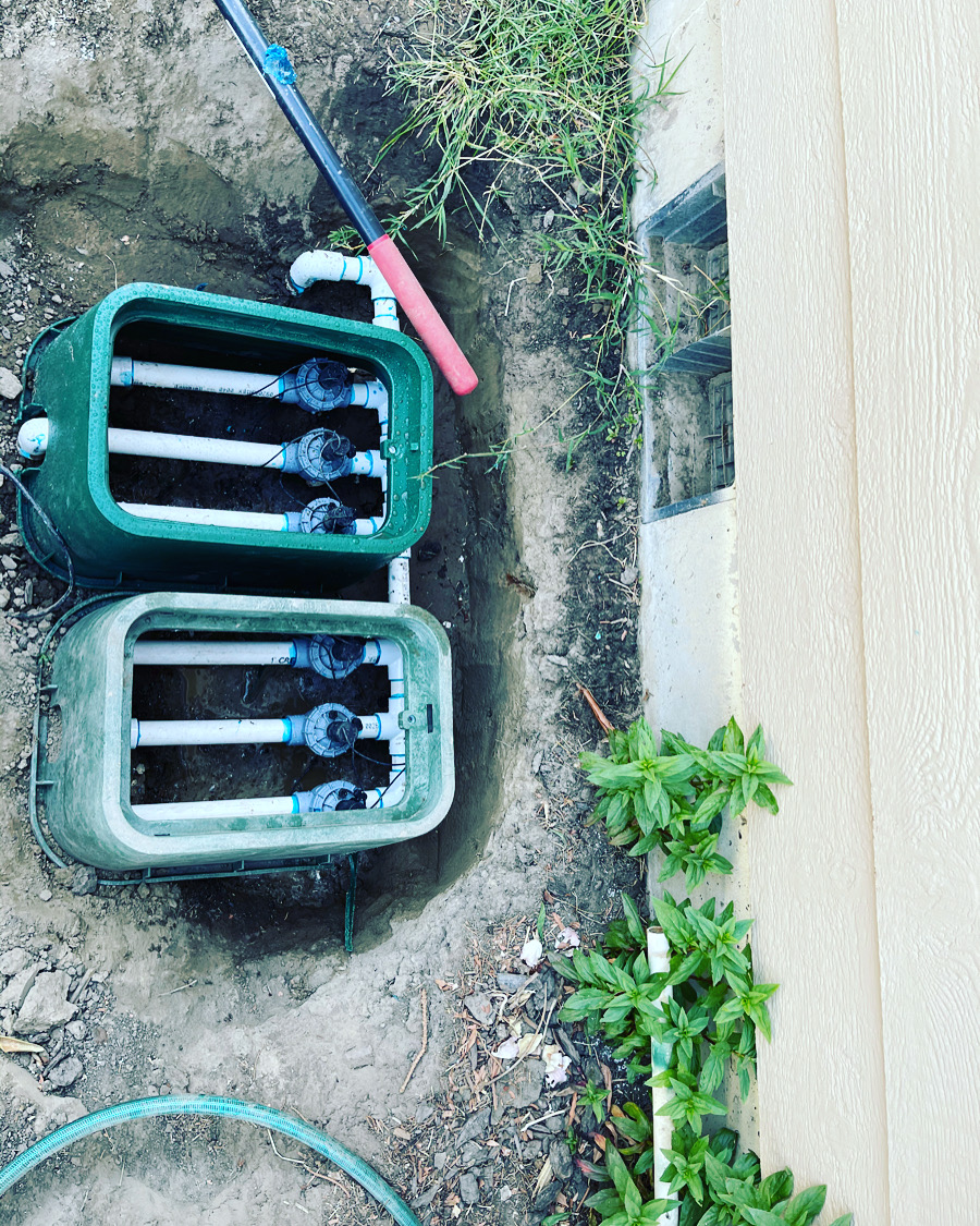 Two green valve boxes freshly installed next to a house foundation