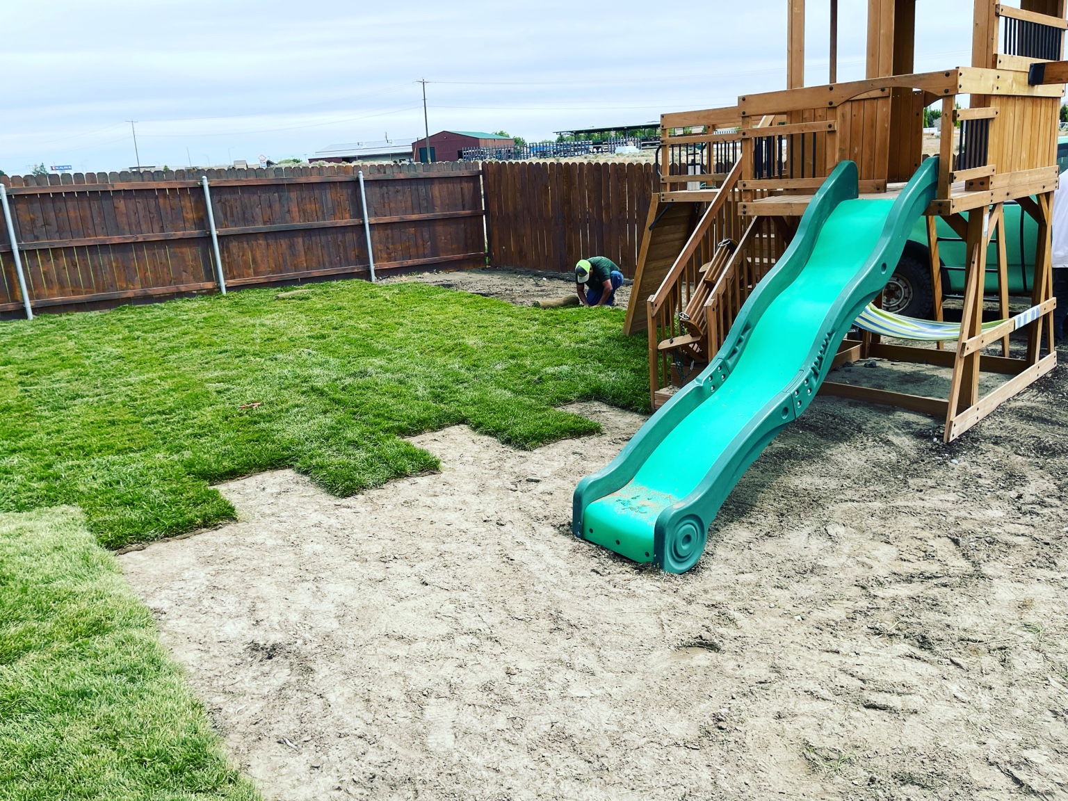 Fresh sod being laid in a backyard around a playground and swing set