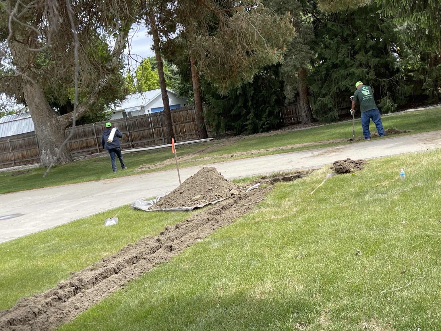 Two-person crew hand-finishing a trench across a residential lawn
